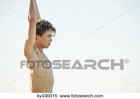 Stock Photography - Shirtless man standing with arms raised. Fotosearch