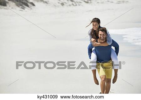 Man giving piggyback ride to his wife on the beach View Large Photo Image Stock Photo - Man giving piggyback ride to his wife on the beach. Fotosearch