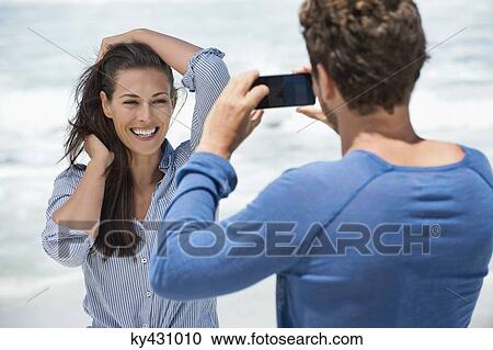 Man taking a picture of his wife with a cell phone on the beach View Large Photo Image Stock Image - Man taking a picture of his wife with a cell phone on the beach. Fotosearch