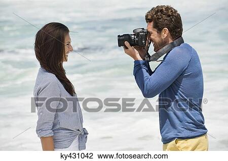 Man taking a picture of his wife with a camera on the beach View Large Photo Image Stock Image - Man taking a picture of his wife with a camera on the beach. Fotosearch