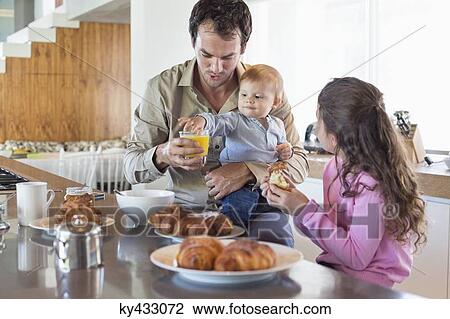 Stock Image - Family having breakfast at a kitchen counter. Fotosearch