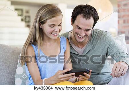 Father and daughter playing a video game and smiling at home View Large Photo Image Picture - Father and daughter playing a video game and smiling at home. Fotosearch