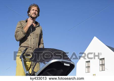 Stock Image - Low angle view of a man standing with a baby stroller. Fotosearch