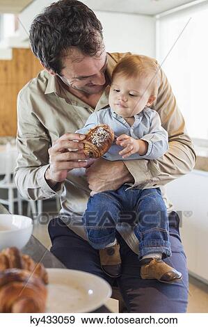 Man feeding bread to his son at a kitchen counter View Large Photo Image Stock Photo - Man feeding bread to his son at a kitchen counter. Fotosearch