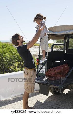 Stock Photography - Man playing with his daughter beside a SUV. Fotosearch