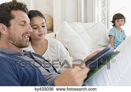 Man reading a magazine with his daughter and his son in the background View Large Photo Image Stock Photograph - Man reading a magazine with his daughter and his son in the background. Fotosearch
