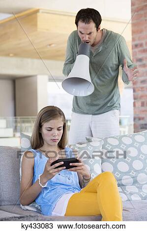 Stock Image - Man shouting into a megaphone at his daughter for playing video game. Fotosearch