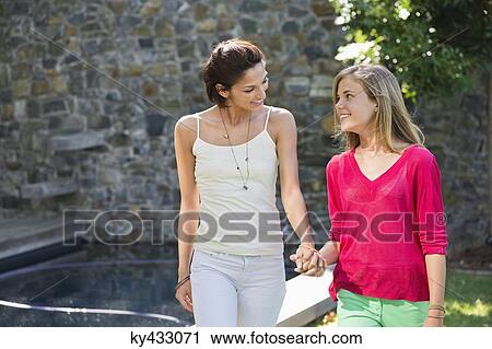 Stock Image - Smiling mother and daughter walking and holding each other's hands. Fotosearch