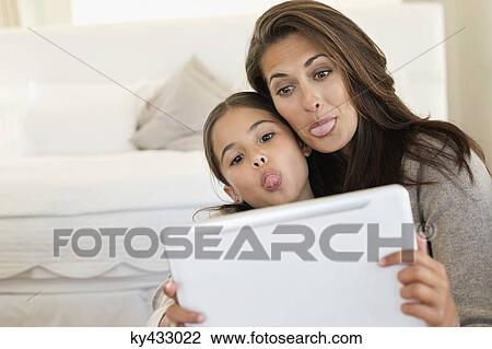 Woman and her daughter making their faces in front of digital tablet View Large Photo Image Stock Image - Woman and her daughter making their faces in front of digital tablet. Fotosearch
