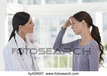 Female patient gesturing headache while discussing with a doctor View Large Photo Image Stock Image - Female patient gesturing headache while discussing with a doctor. Fotosearch