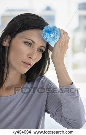 Woman holding a water bottle on her forehead View Large Photo Image Picture - Woman holding a water bottle on her forehead. Fotosearch