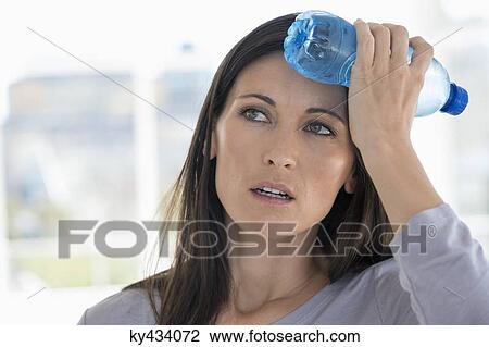 Stock Image - Woman holding a water bottle on her forehead. Fotosearch