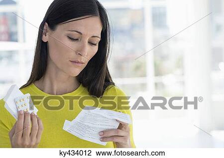 Stock Image - Woman reading instructions before taking medicine. Fotosearch