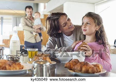 Girl having breakfast beside her mother at a kitchen counter View Large Photo Image Stock Photo - Girl having breakfast beside her mother at a kitchen counter. Fotosearch