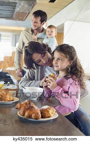 Stock Photography - Girl having breakfast beside her mother at a kitchen counter. Fotosearch