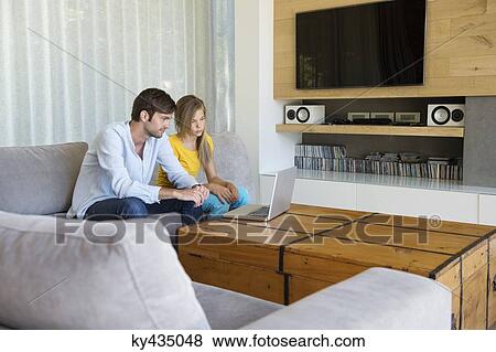 Man and his daughter sitting on a couch looking at a laptop View Large Photo Image Stock Photo - Man and his daughter sitting on a couch looking at a laptop. Fotosearch