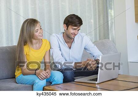 Man and his daughter sitting on a couch looking at a laptop View Large Photo Image Stock Photography - Man and his daughter sitting on a couch looking at a laptop. Fotosearch