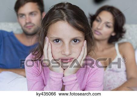 Portrait of a girl looking upset with her parents in the background View Large Photo Image Stock Photograph - Portrait of a girl looking upset with her parents in the background. Fotosearch