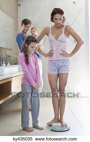 Woman measuring her weight on a weighing scale with her family in bathroom View Large Photo Image Stock Photography - Woman measuring her weight on a weighing scale with her family in bathroom. Fotosearch