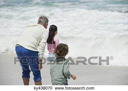 Stock Image - Children with their grandfather looking at surf on the beach. Fotosearch