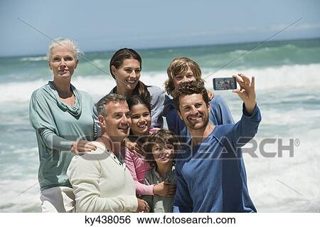Stock Photograph - Happy multi-generation family taking a self portrait with a cell phone on the beach. Fotosearch