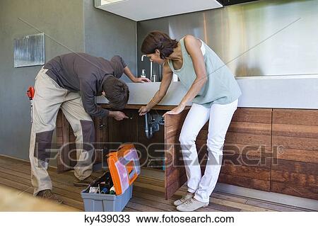 Man examining a kitchen sink with a woman standing beside him View Large Photo Image Stock Image - Man examining a kitchen sink with a woman standing beside him. Fotosearch