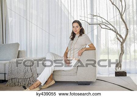Portrait of a beautiful woman sitting on a couch View Large Photo Image Stock Photography - Portrait of a beautiful woman sitting on a couch. Fotosearch