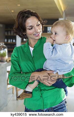 Stock Photography - Woman carrying her son and smiling at home. Fotosearch