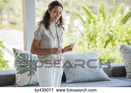 Stock Photo - Woman holding stem glasses and smiling at home. Fotosearch