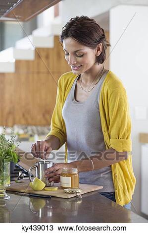Stock Image - Woman preparing herbal tea in the kitchen. Fotosearch