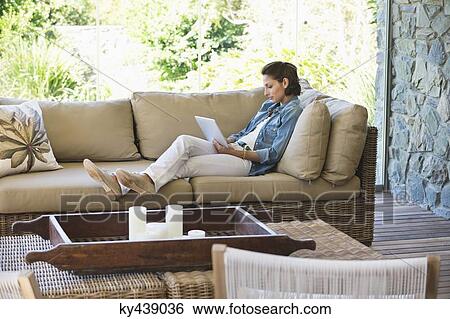 Woman reclining on a couch and using a digital tablet View Large Photo Image Stock Photograph - Woman reclining on a couch and using a digital tablet. Fotosearch