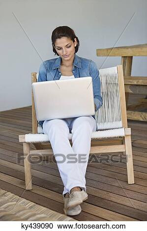 Woman sitting on a chair and using a laptop View Large Photo Image Stock Image - Woman sitting on a chair and using a laptop. Fotosearch
