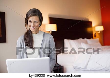 Woman using a laptop in a hotel room and smiling View Large Photo Image Stock Image - Woman using a laptop in a hotel room and smiling. Fotosearch