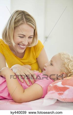 Smiling woman looking at her daughter lying on the bed View Large Photo Image Stock Photo - Smiling woman looking at her daughter lying on the bed. Fotosearch