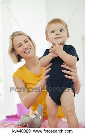 Stock Photo - Smiling woman playing with her baby on the bed. Fotosearch