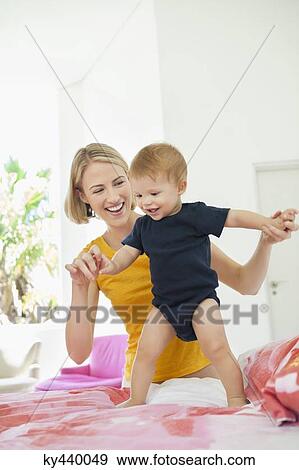 Smiling woman playing with her baby on the bed View Large Photo Image Stock Photo - Smiling woman playing with her baby on the bed. Fotosearch