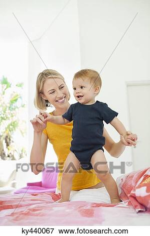 Stock Photo - Smiling woman playing with her baby on the bed. Fotosearch
