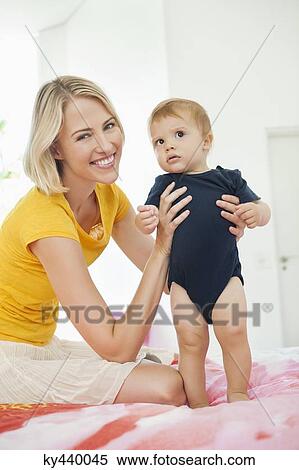 Stock Photography - Smiling woman playing with her baby on the bed. Fotosearch