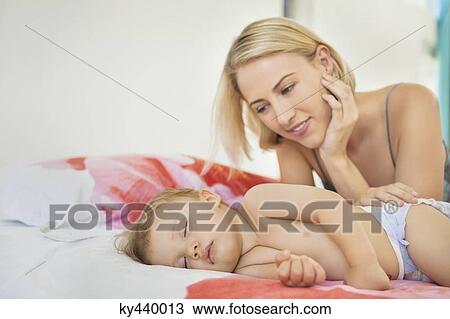 Stock Image - Woman looking at her baby sleeping on the bed. Fotosearch