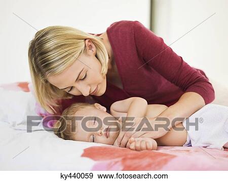Stock Photo - Woman looking at her baby sleeping on the bed. Fotosearch