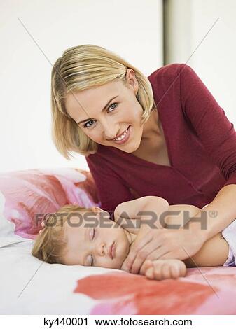 Stock Image - Woman near her baby sleeping on the bed. Fotosearch