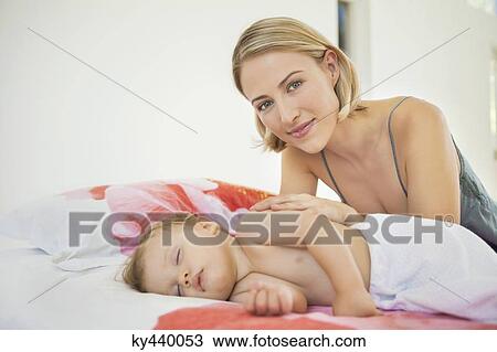 Woman sitting near her baby sleeping on the bed View Large Photo Image Stock Image - Woman sitting near her baby sleeping on the bed. Fotosearch