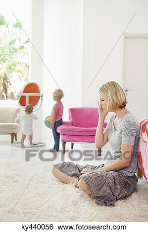 Woman sitting on a rug with her children playing in the background View Large Photo Image Stock Photograph - Woman sitting on a rug with her children playing in the background. Fotosearch