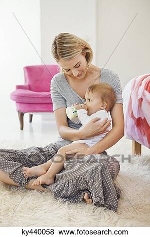 Woman sitting with her baby feeding with a baby bottle View Large Photo Image Stock Photo - Woman sitting with her baby feeding with a baby bottle. Fotosearch