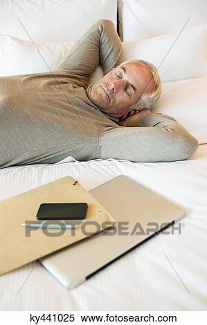 Man resting on the bed with a laptop and file in a hotel room View Large Photo Image Stock Photography - Man resting on the bed with a laptop and file in a hotel room. Fotosearch