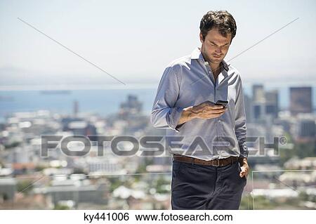 Man standing on the terrace using a mobile phone View Large Photo Image Stock Photograph - Man standing on the terrace using a mobile phone. Fotosearch