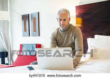 Man using a laptop in a hotel room View Large Photo Image Stock Image - Man using a laptop in a hotel room. Fotosearch