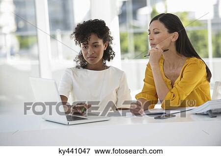 Two female friends looking at a laptop at home View Large Photo Image Stock Photo - Two female friends looking at a laptop at home. Fotosearch