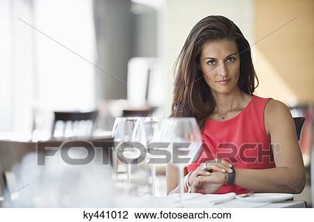 Stock Image - Woman sitting in a restaurant and looking at wristwatch. Fotosearch