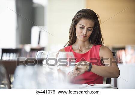 Woman sitting in a restaurant and looking at wristwatch View Large Photo Image Stock Photograph - Woman sitting in a restaurant and looking at wristwatch. Fotosearch